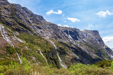 Fototapeta na wymiar Small waterfalls from sheer cliffs on the way to Fiordland. South Island, New Zealand