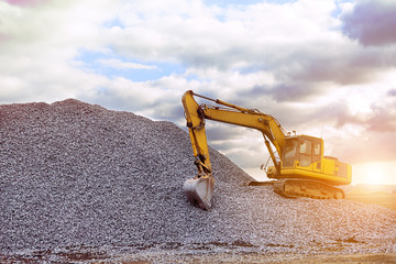 crawler excavator in the rays of the setting sun at sunset digs earth and sand at a construction...