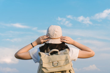 Fototapeta premium woman traveler with backpack holding hat and looking at the blue sky, travel concept, space for text and atmospheric moment