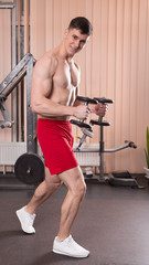 Young man flexing muscles with barbell in gym.