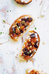 Sandwich (bruschetta) with Italian caponata (fried vegetable ragout) and cream cheese on frayed rustic background.