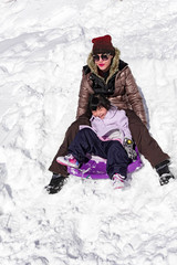 Fototapeta na wymiar Child while enjoying playing with snow and sliding with mommy