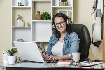 Happy adult woman in headphones using laptop with pleasure at home
