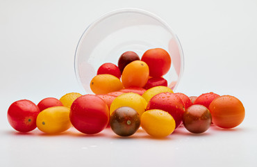 Colorful cherry tomatoes (red, garnet and yellow), fresh and raw. In plastic jar. Isolated on white background