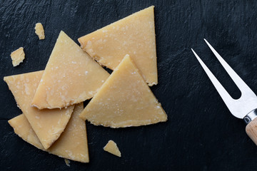 Cured sheep cheese. Cut into pieces on black board. Cheese fork. Top View.