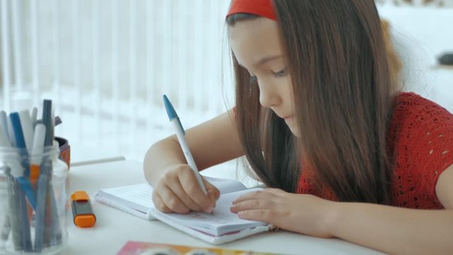 Bella niña de rojo escribe con cuidado y su bolígrafo  en su diario
