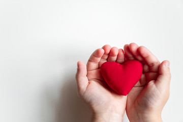 Fototapeta premium Close up child hand holding red heart on light background top view with copy space