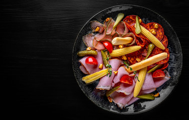 plate with meat, salami, ham on black wooden table background