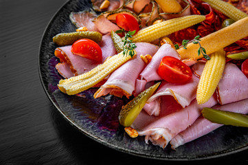 plate with meat, salami, ham on black wooden table background