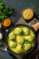 Meatballs with bulgur in sour cream and turmeric sauce in a pan on a dark stone countertop. Top view flat lay background. Copy space.