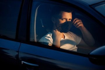 Portrait of man wearing disposable medical facemask in a car during coronavirus outbreak. Safety in the city.