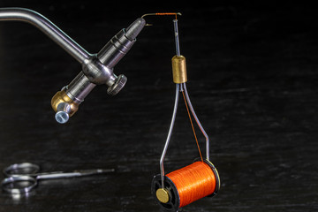 bobbin of thread hanging from a hook on a fly tying vise