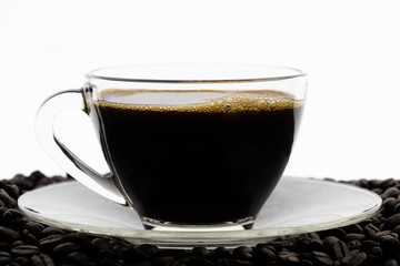 Black coffee with foam in clear glass cup on coffee beans field with white background