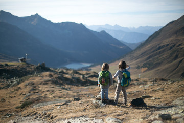 Two children with backpacks in high mountains holding hands looking into the distance