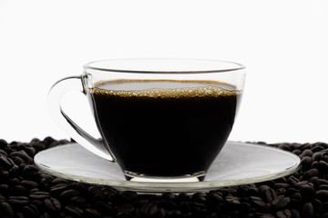 Black coffee with foam in clear glass cup on coffee beans field with white background