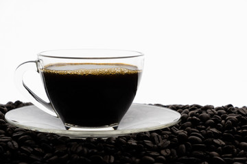 Black coffee with foam in clear glass cup on coffee beans field with white background