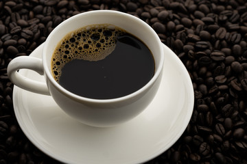 Hot black coffee with foam in a white coffee cup on coffee beans field background