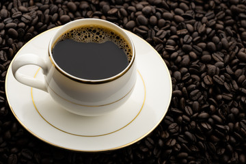 Hot black coffee with foam in a white coffee cup on coffee beans field background