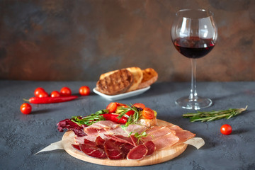 Assorted meat delicacies, cut into thin slices on a round wooden Board. Decorated with bruschetta with vegetables and fresh herbs