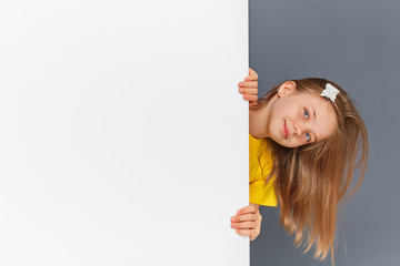 Funny teen girl in yellow clothes looks over a white wall sign.