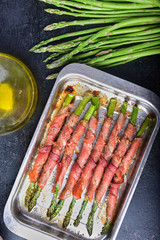 green asparagus with ham cooked on a black background and surrounded by ingredients.