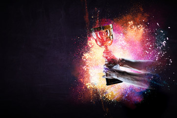 Hand holding up a gold trophy cup against dark background