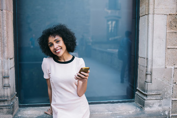 Happy young ethnic woman using smartphone in street