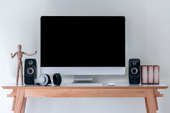 Mockup desktop computer with black screen with speakers and headphone on wooden table.