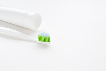 Toothbrush with green bristles and white tube of toothpaste on light gray table background. Teeth hygiene concept. Empty place for text or logo. Closeup.