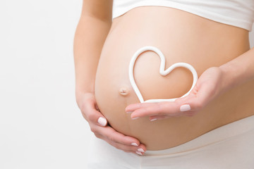 Young woman hand holding white heart shape on naked belly. Emotional loving moment in pregnancy time - 30 weeks. Baby expectation. Love, happiness and safety concept. Closeup. - obrazy, fototapety, plakaty
