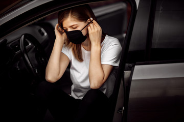 Fototapeta na wymiar Beautiful young girl in a mask sitting in a car, protective mask against coronavirus, driver on a city street during a coronavirus , covid-19