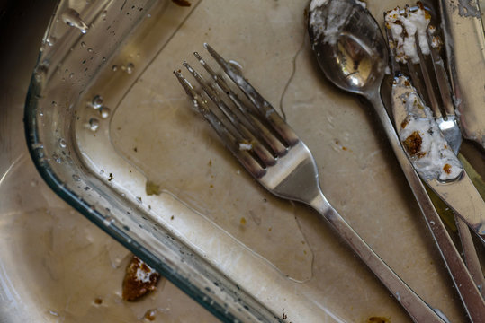 dirty fork knife and spoon covered with icing under water inside kitchen sink