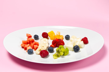 Fresh fruit salad on white plate. Mixed fruit in white plate healthy food style. Useful fruit salad of fresh fruits and berries on pink background