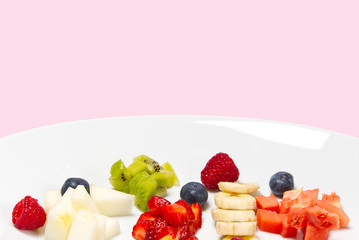 Fresh fruit salad on white plate. Mixed fruit in white plate healthy food style. Useful fruit salad of fresh fruits and berries on pink background