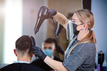 Fototapeta premium Hairdresser with security measures for Covid-19, blow-dry a man in a medicine mask, social distance, cutting hair with a medical mask, eye mask and rubber gloves in a beauty salon