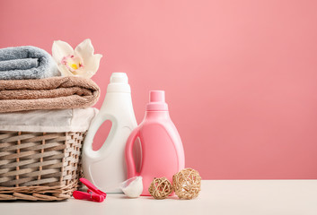 Obraz na płótnie Canvas Wicker laundry basket with towels and orchid flower, detergents, washing powrder on pink background