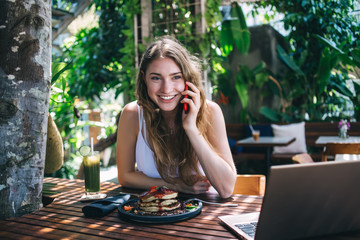 Cheerful young woman communicating via smartphone during breakfast