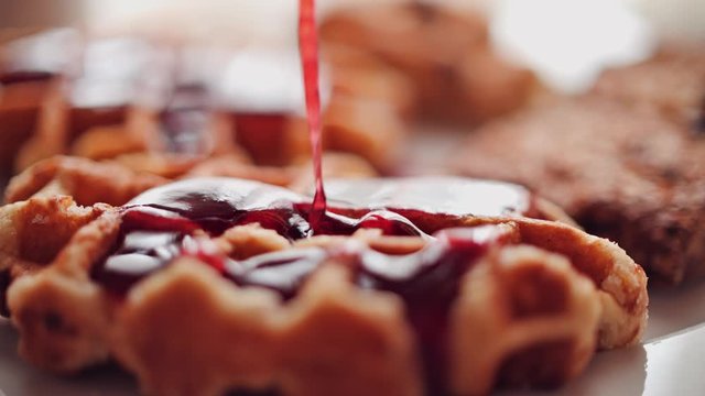 Pouring red dessert berry sauce over waffle, close-up shot