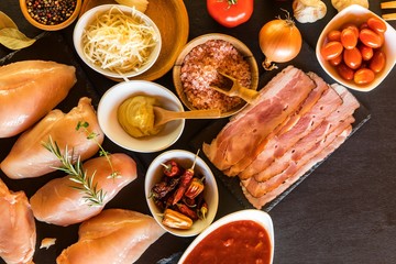 Raw chicken and bacon on the table top. Ingredients for healthy food. Chicken breast with tomatoes.