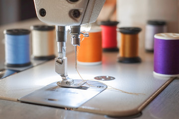 Needle presser foot of industrial sewing machine for sew cloth with colorful thread roll close-up.