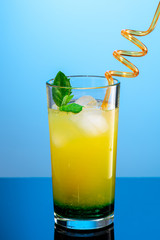 cocktail of orange juice, mint syrup and ice in a direct glass on a blue background