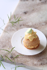 Contemporary key lime choux buns with craquelin, dipped in white chocolate, decorated with whipped diplomat cream and meringue cookies, on a marble board.