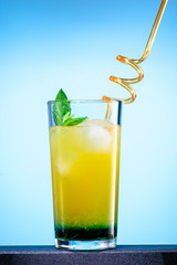 cocktail of orange juice, mint syrup and ice in a direct glass on a blue background