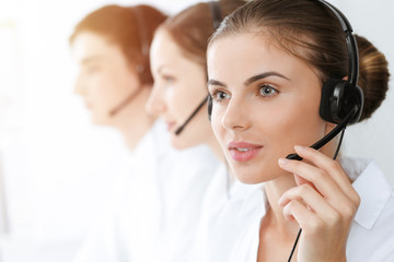 Call center. Beautiful young woman using headset and computer to help customers in sunny office. Business concept