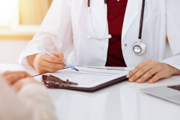 Unknown woman-doctor consulting patient and using clipboard with a medication history record in sunny room. Medicine concept