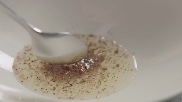 Slow motion mix spices with grapeseed oil in white bowl closeup