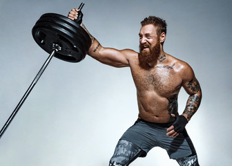 Strong man does landmine exercises, workout with barbell. Photo of sporty man on grey background....