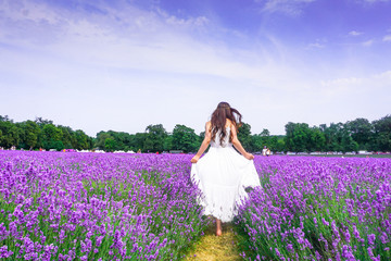 A young woman with dark hair wearing a long white dress with a big summer hat in a lavender field