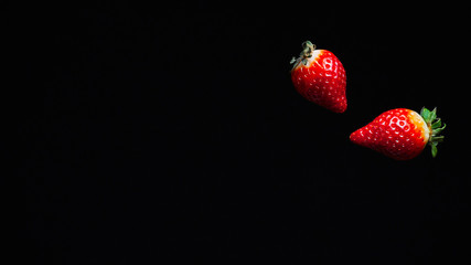 two ripe juicy red strawberries fly fall in the air on a dark background