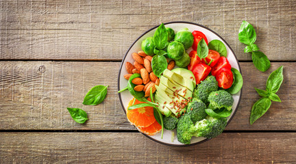 Avocado salad with tomatoes, cabbage, spinach, oranges, flax and pumpkin seeds in plate on wooden background. Top view.
